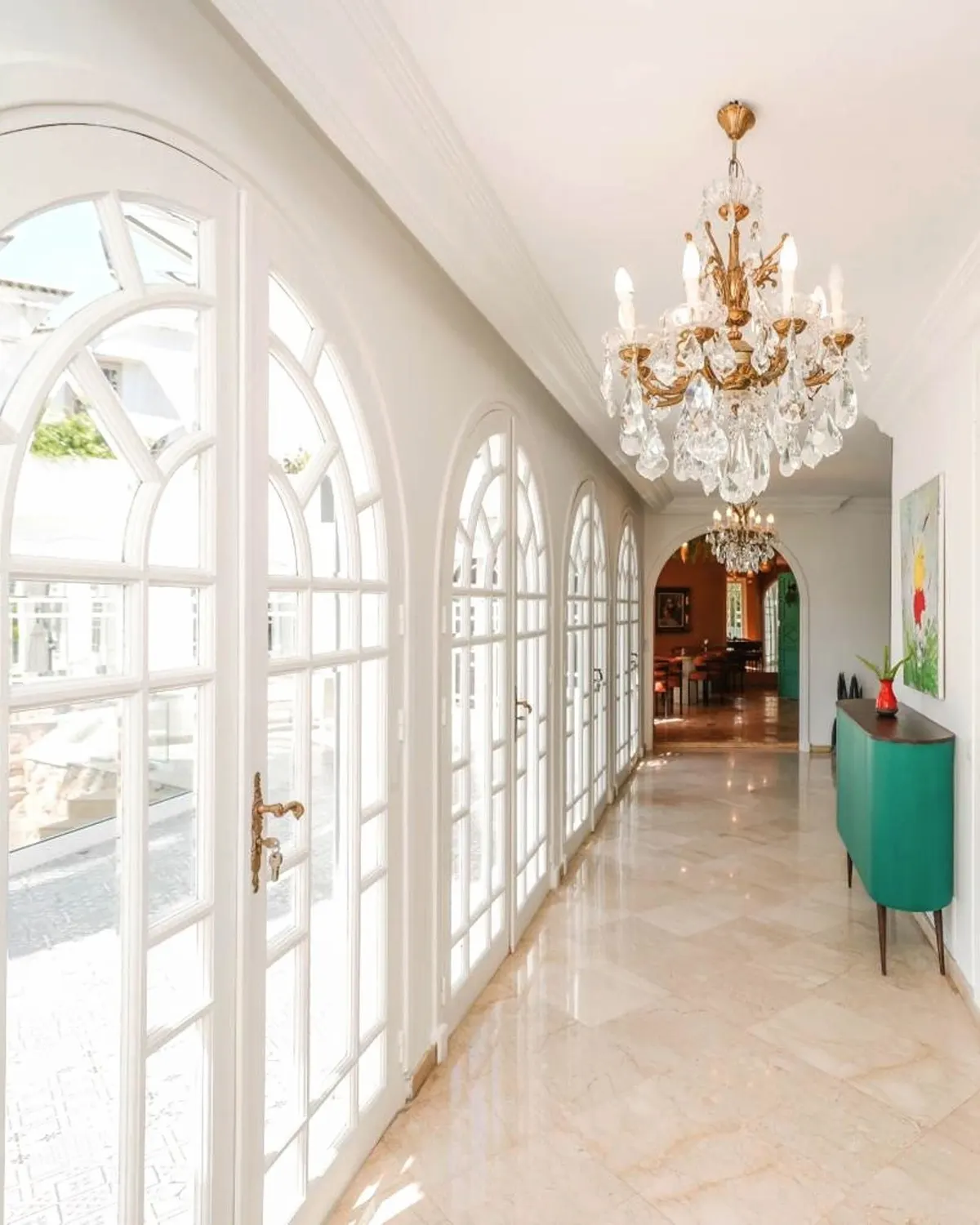 The gallery of La Résidence: a row of arched French windows, a crystal chandelier and a marble floor along the garden front.