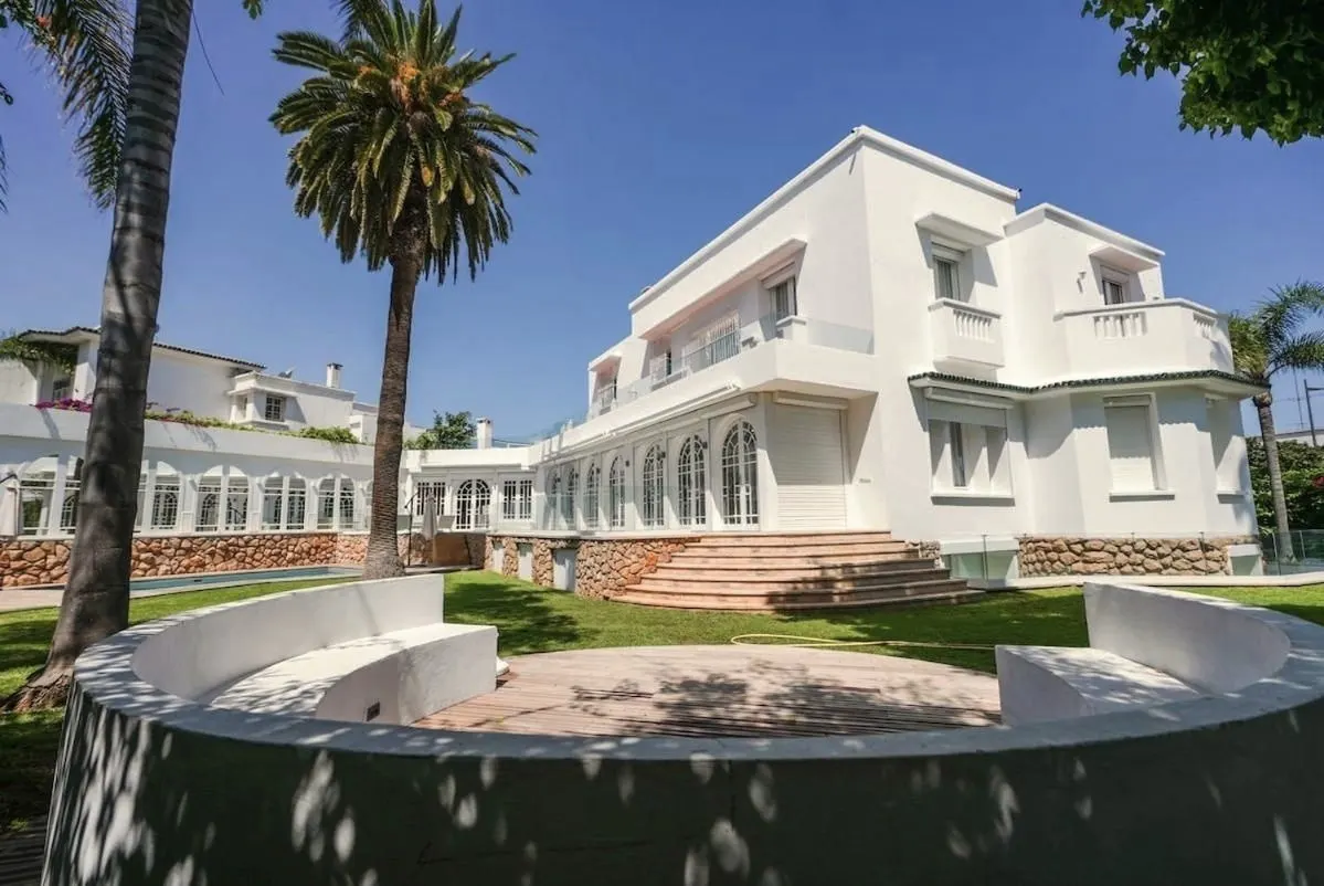 The front of the villa with a round stone basin and palms.