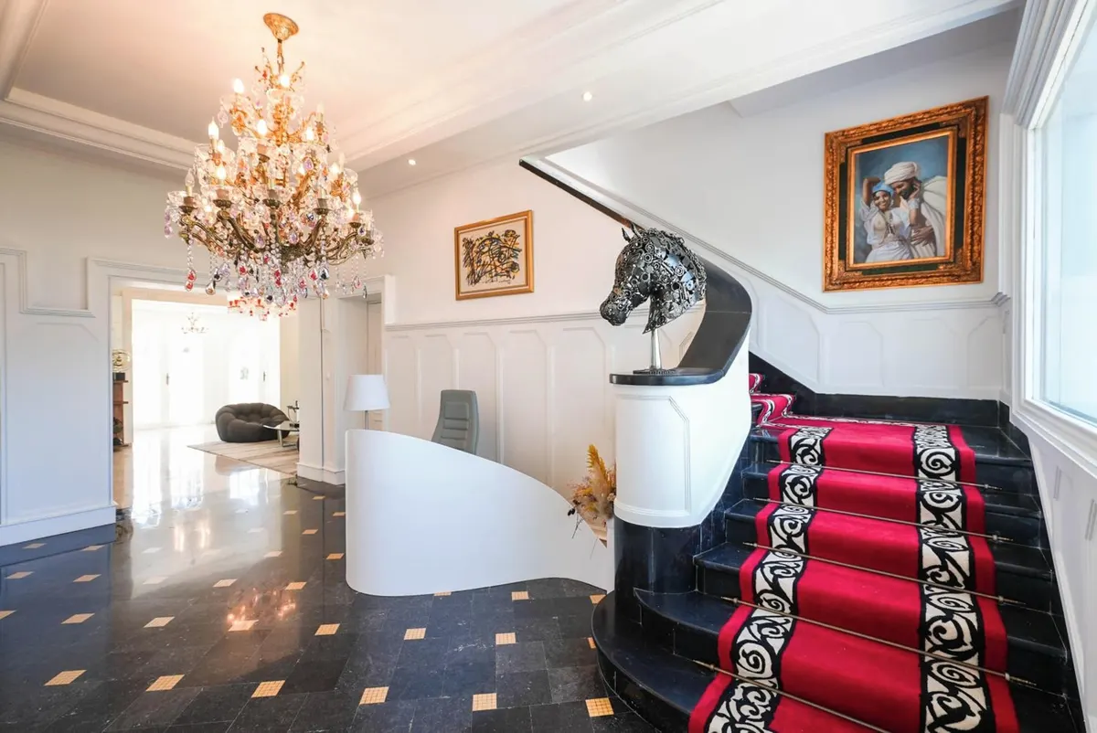 The hall: black-and-white marble floor, a curved white stair on a red runner, a crystal chandelier.