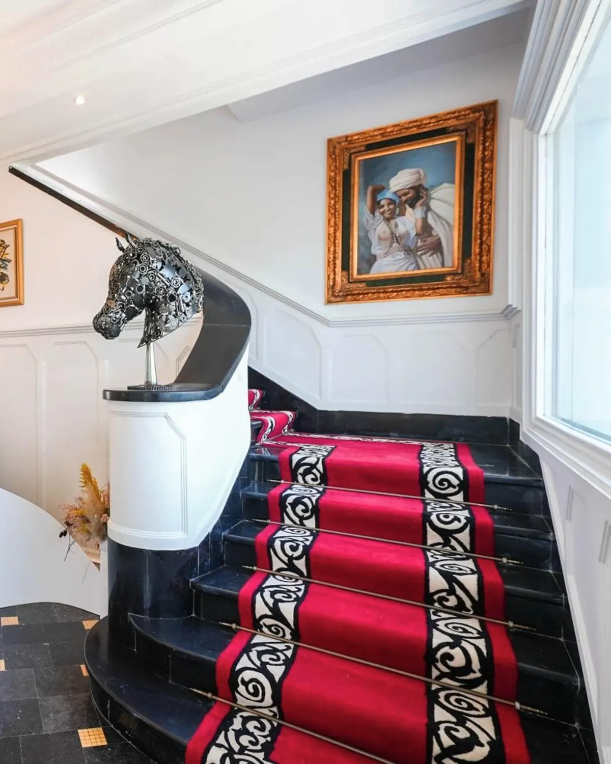 The hall: black-and-white marble floor, a curved white stair on a red runner, a crystal chandelier.