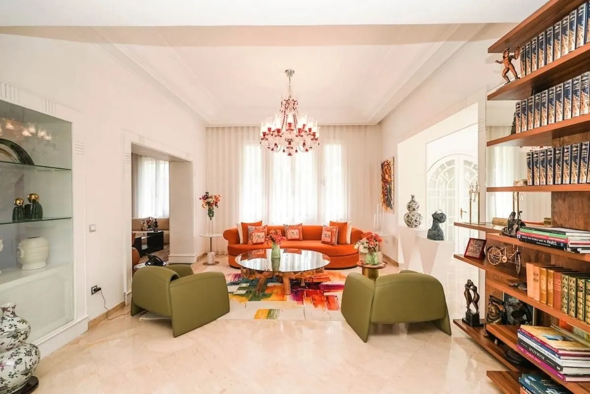 The library opening onto a salon of orange velvet sofas, under a crystal chandelier.