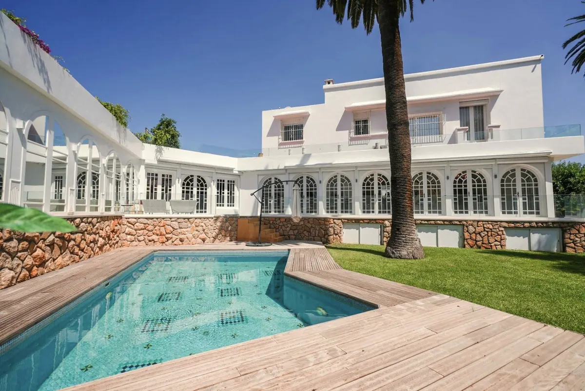 The mosaic pool, the timber deck, the stone wall and the villa’s arcade of French windows.