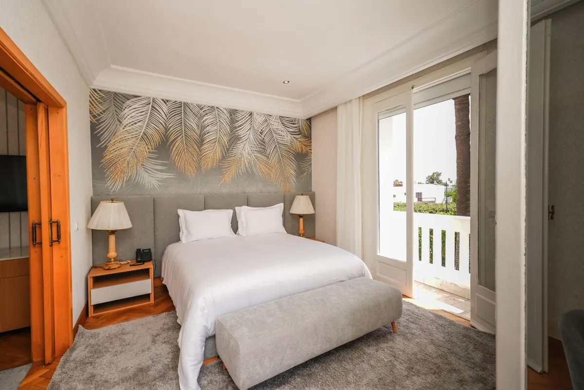 Family Studio: bedroom with a leaf mural and French windows to a white balcony over the palms.