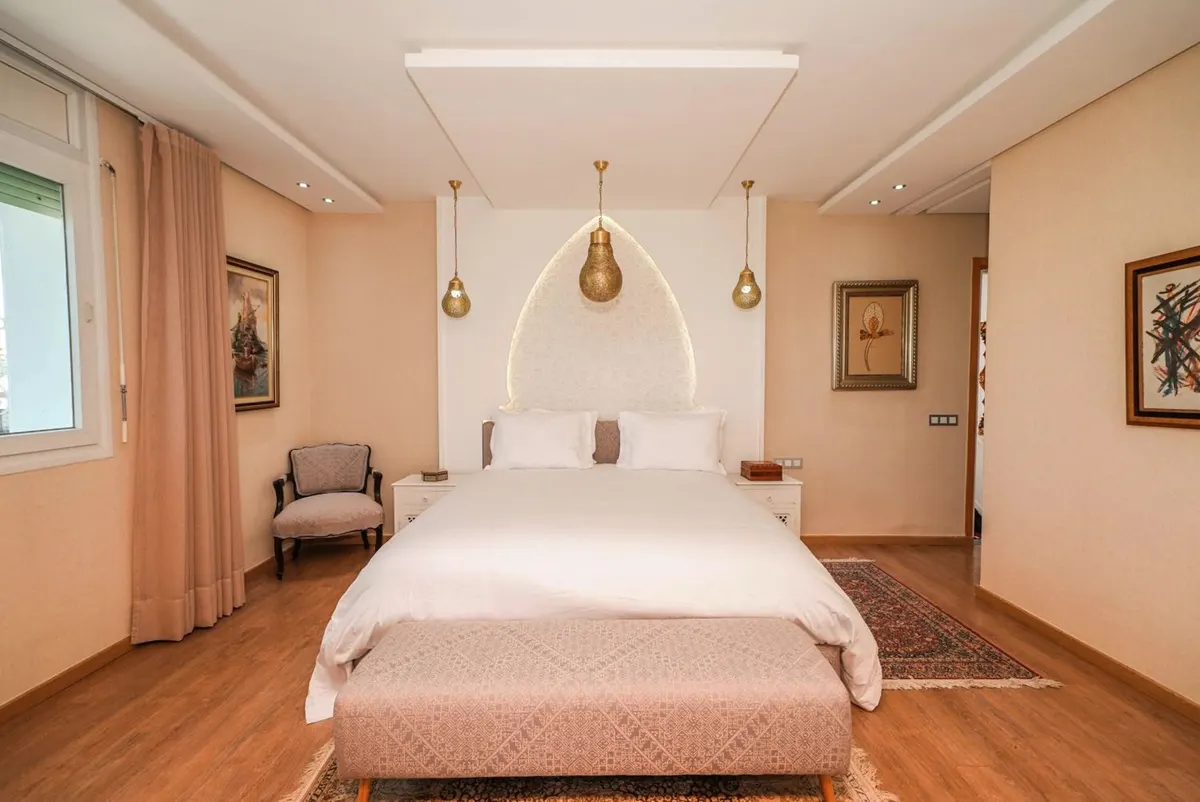 Deluxe Suite: white bed under an arched plaster niche and brass pendant lamps.